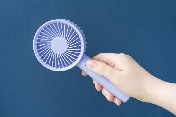 istock Female hand holding mini fan on blue background close-up. 2159622472