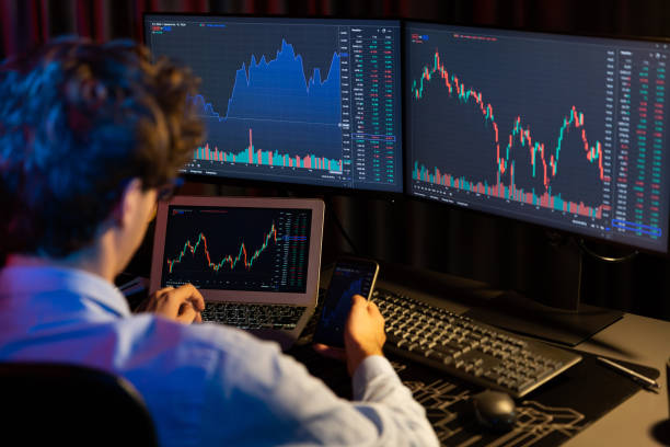 istock Young investor stock trader holding smartphone comparing with screens. Gusher. 2159623192
