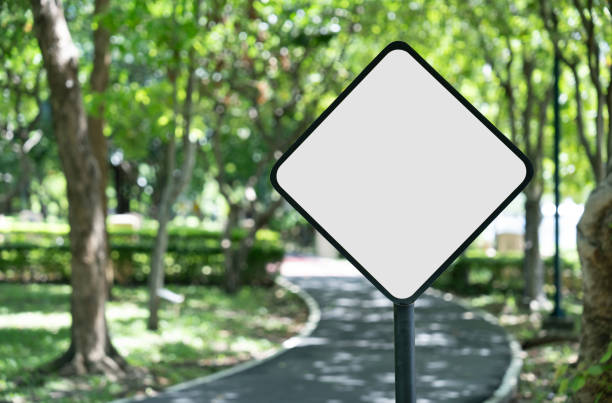The image shows a mock-up warning sign with a white background against a blurred backdrop of a green garden and road.