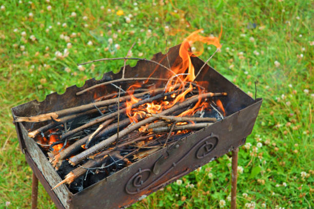 Building a bonfire inside a metal rectangular brazier. Firewood is burning for barbecue on the street.charcoal briquettes and fire sticks