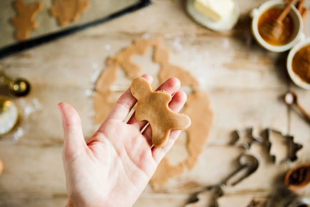 Hand holding freshly cut gingerbread man cookie shape from dough over the kitchen counter. Woman making gingerbread man shape Christmas cookies in kitchen.