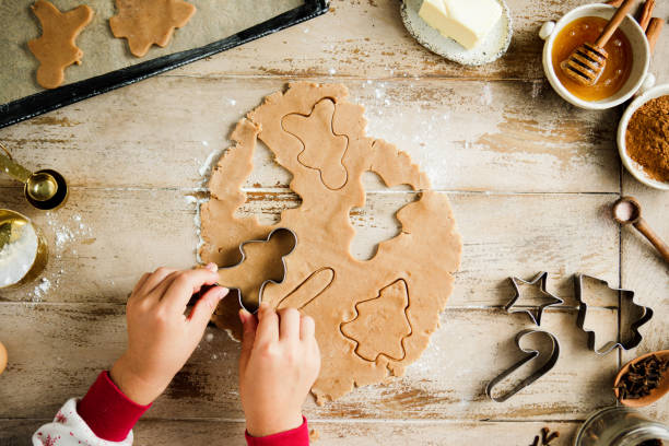 Top view of hands of a child cutting dough with gingerbread man shape cookie cutter. Kid preparing Christmas sweets at table in kitchen.