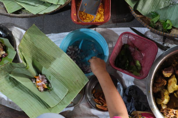 istock Hand preparing seasoned chicken by wrapping it in a banana leaf, surrounded by various ingredients and kitchen tools, high angle view 2159636617