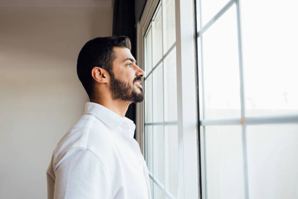 istock Bearded man standing at window and looking at view 2159639744