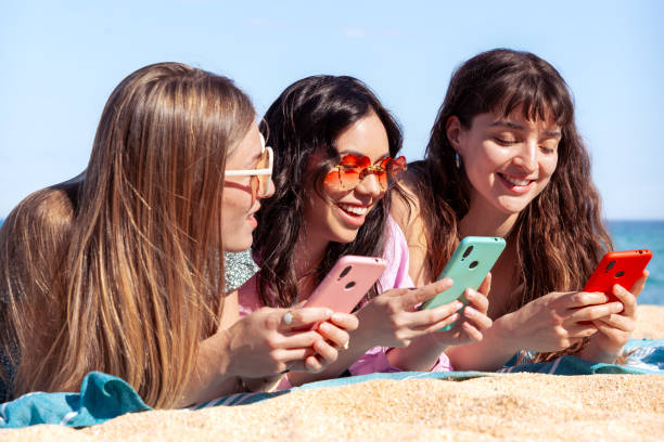 istock Three happy young friends on the beach using apps on their smartphones. 2159641698