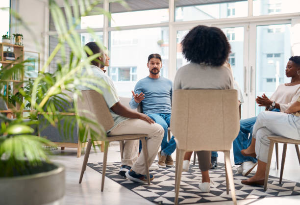 istock Diverse group of individuals participating in a support group session inside a bright room with large windows. The group sits in a circle, engaging in open discussion and offering mutual support. 2159641895