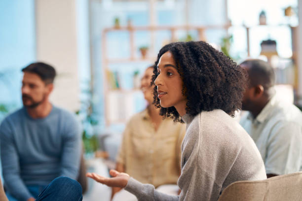 istock A diverse group of individuals participating in a support group meeting. A woman speaks while others listen attentively, creating a warm and encouraging atmosphere. Ideal for concepts of community, support, and mental health. 2159641941
