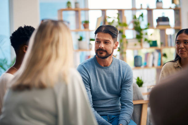 A diverse group of individuals engaged in a support group session, focusing on personal sharing and emotional support in a welcoming environment. Participants are engaged in conversation and actively listening to one another.