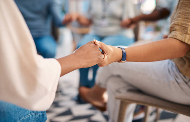 A diverse group of individuals hold hands during a support group session. The image conveys themes of unity, community, and emotional support. Perfect for topics related to mental health, empathy, and human connection. stock photo