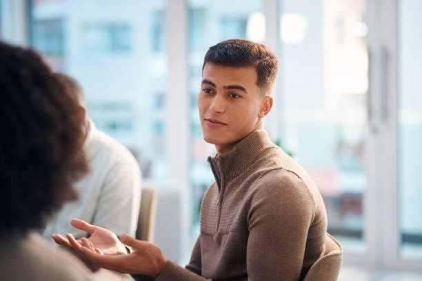 istock A young man participates in a diverse support group meeting. The group sits together in a bright and casual setting, fostering a sense of community, understanding, and emotional support. 2159641964