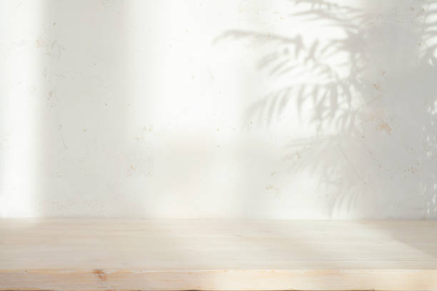istock Bleached empty wooden table top with leaves shadow on abstract stucco wall texture background 2159644396