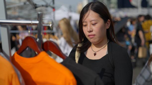 Asian woman looking for second hand clothing in flea market