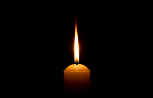 istock Single burning candle flame or light glowing on a big white candle on black or dark background on table in church for Christmas, funeral or memorial service with copy space. 2159651760
