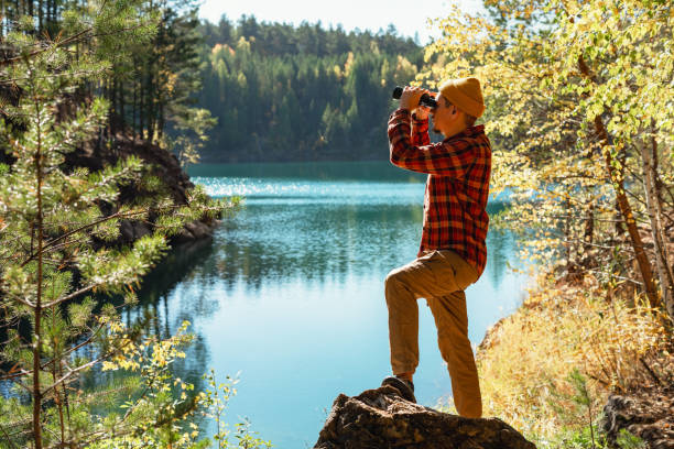 istock Young man looking through binoculars at birds on lake in fall Birdwatching, zoology, ecology. Research in nature, observation of animals Ornithology 2159653070
