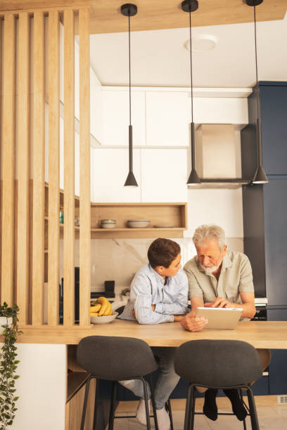 istock Grandfather using tablet PC beside grandson in kitchen 2159653506