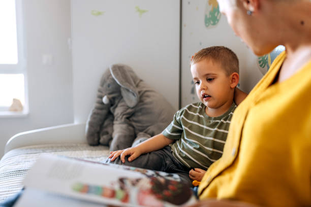 istock Mother and son reading book while sitting on a bed in child's room 2159656068