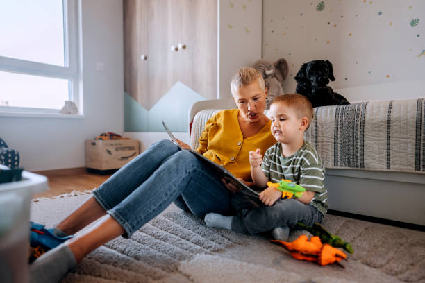 istock Mother and son reading book while sitting on a floor at home 2159656146