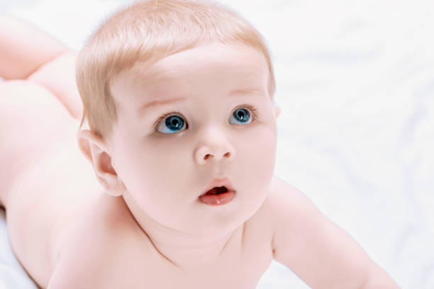 Newborn baby with big blue eyes lays on a white blanket, looking up with curiosity and wonder, radiating hope and promise for the future