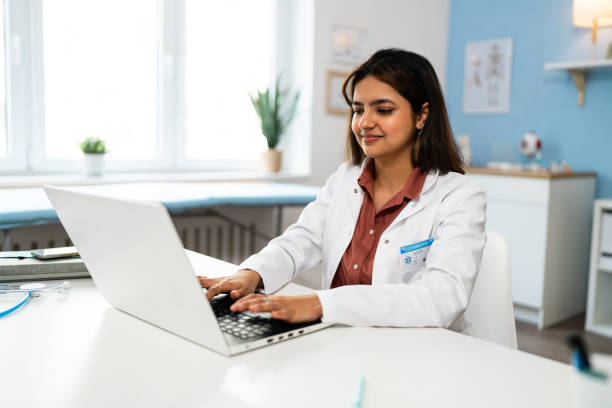 Female doctor Indian ethnicity working on laptop at the ordination Female doctor of Indian ethnicity working on laptop at the modern ordination medical occupation stock pictures, royalty-free photos & images