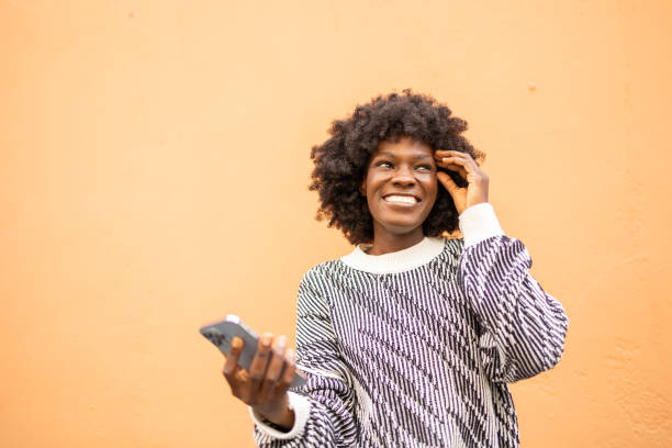 istock Smiling woman with smartphone against peach wall background 2159666575
