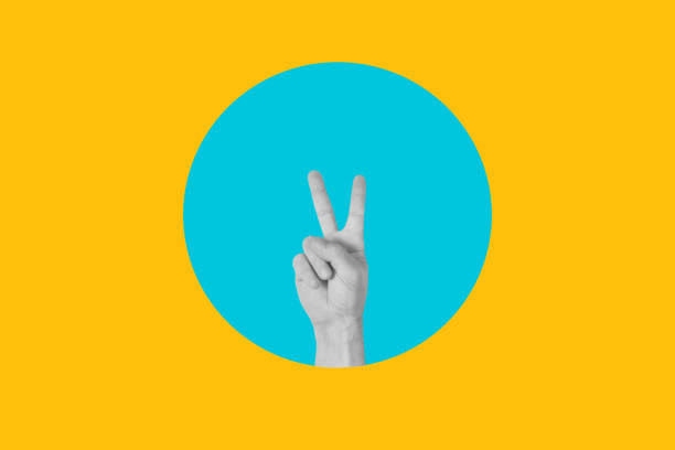 istock Man hand with victory gesture on a blue circle on a yellow background 2159677772