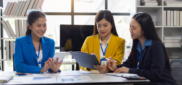 istock Three Asian businesswomen discuss presenting a new project idea. Analyze financial and investment market planning and statistics at the office using tablet pc and smiling. 2159682350