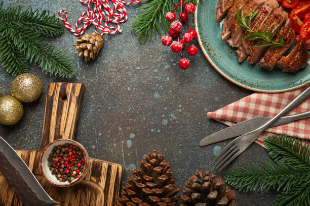 istock Festive Christmas dinner boarder background with space for text with roasted duck breast fillet with golden crispy skin and tomato salad, Xmas decorations with fir tree, cones, red berries 2159685793