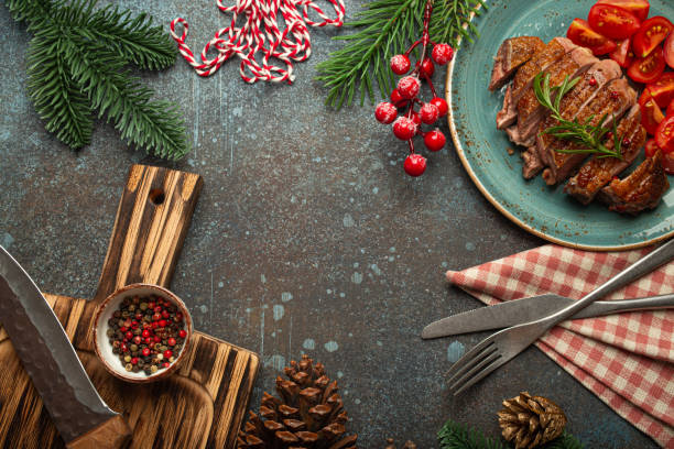 istock Festive Christmas dinner boarder background with space for text with roasted duck breast fillet with golden crispy skin and tomato salad, Xmas decorations with fir tree, cones, red berries 2159685801