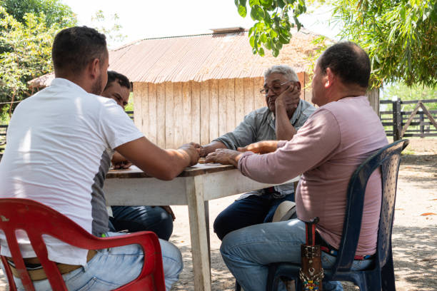 Four men engaged in a game of dominoes at an outdoor table near a rustic wooden building.