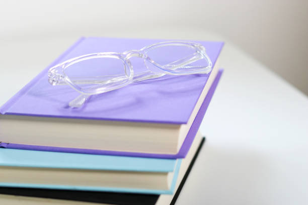Close up mock up books stack and transparent glasses on top on white table with free copy space