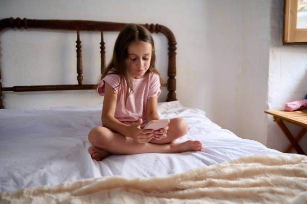 istock Young girl sitting on bed using smartphone in cozy room 2159688584
