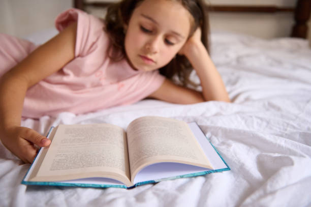 istock Young girl reading a book while lying on a bed 2159688659