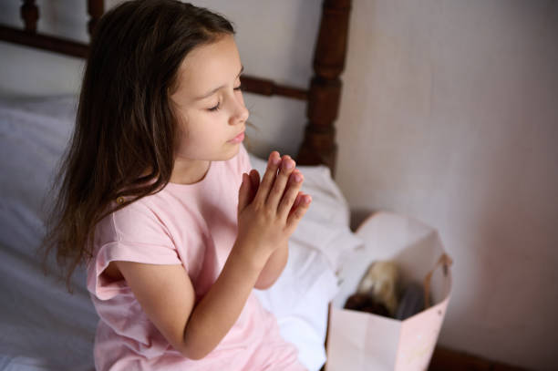 istock Young girl praying on her bed with hands clasped 2159689391