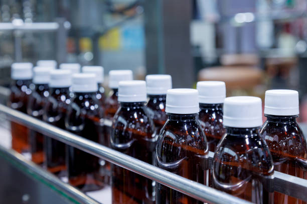 istock glass bottle with white cap moving on conveyor belt of auto capping and labeling machine at energy drink beverage manufacturing. pharmaceutical or beverage industry. automation technology machinery. 2159689392