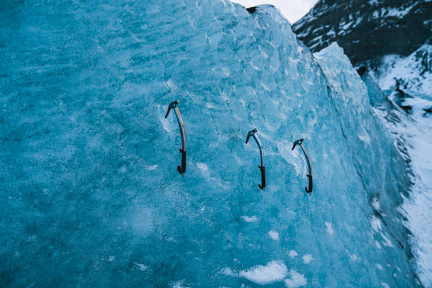 Close-up of ice climbing equipment embedded in a frozen glacier wall, showcasing adventure and extreme sports in a winter landscape.