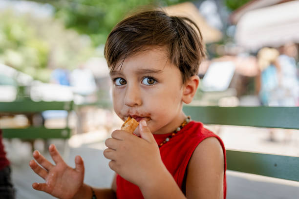 cute boy holding a hot dog in his hands while sitting on a park bench