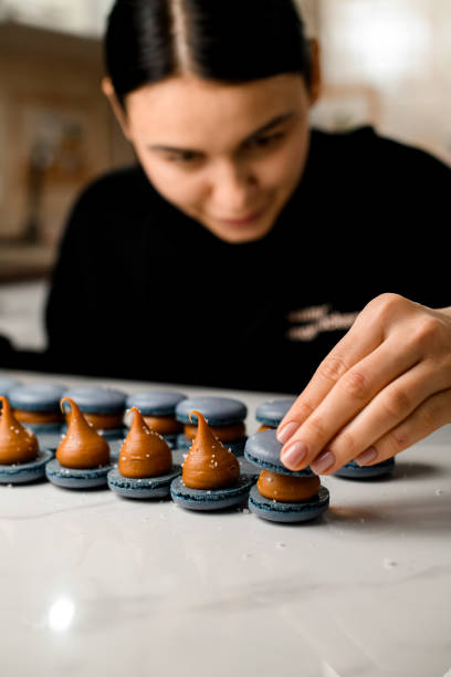 istock Cook chef with dark hair makes a gray blue macarons with brown creamy on a table 2159694387