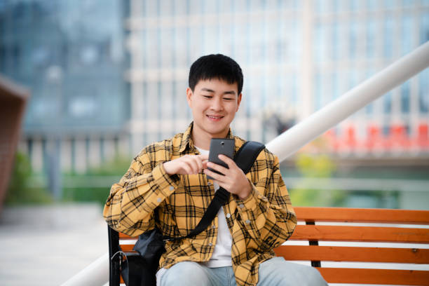 istock Young handsome man using smartphone while sitting on bench on city street 2159695126