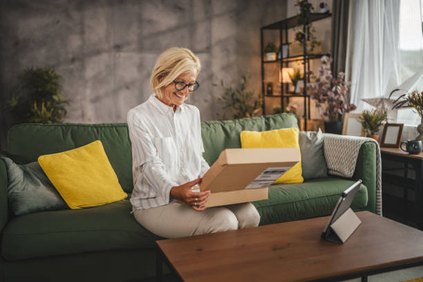 istock Mature sit on sofa woman work from home open delivery package 2159702854