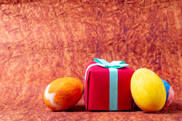 Easter background with colored eggs and red gift box on brown background with copy space. Happy Easter.