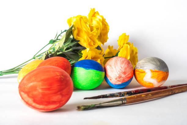 Colorful easter eggs with paint brushes and yellow flowers on a white background. Easter concept.