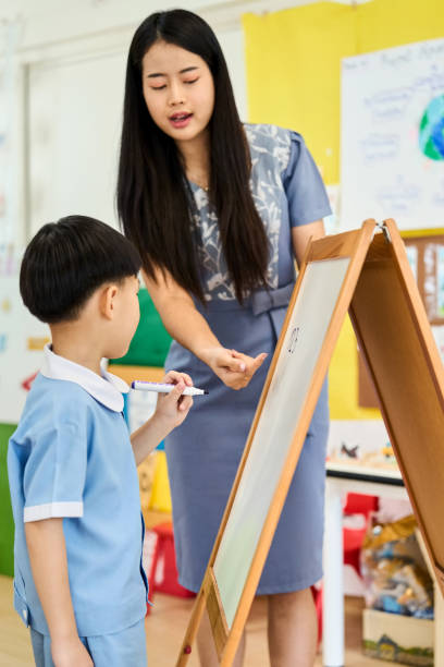 istock Teacher helping boy student write on whiteboard in preschool classroom 2159715004