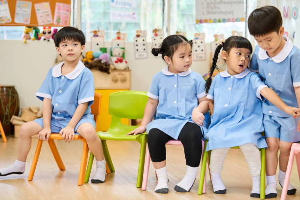 Asian Montessori preschool students sitting on colorful chairs in a row in classroom