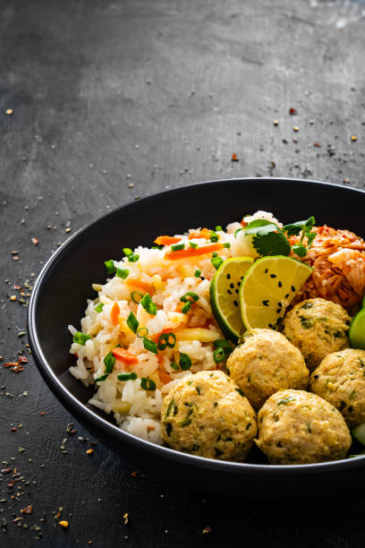 Meatballs served with white rice, marinated sliced cucumber and kimchee on black wooden background