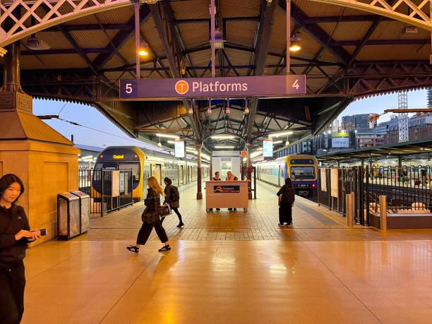 People walking on Central Railway Station concourse in Sydney. There is motion blur from people walking quickly. Two trains are stationary on the platforms.