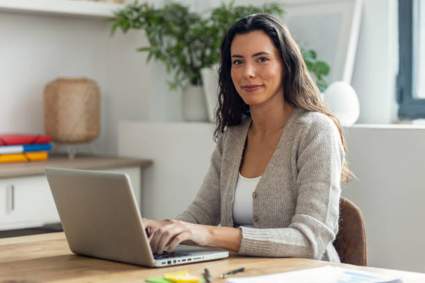 istock Beautiful business woman working while typing with laptop while looking at camera on a desk in the office at home. 2159719181