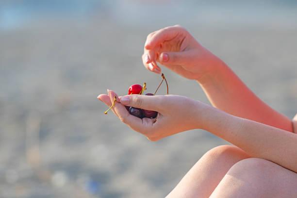 A young girl holding a cherry fruit.