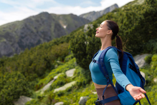 istock Happy lady tourist with backpack is breathing deeply with open arms, reached peak while hiking in mountains hills surrounded by green nature 2159725894