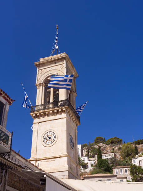 Hydra island church bell tower with greek flags in a sunny day under blue sky, Saronic Gulf, Greece