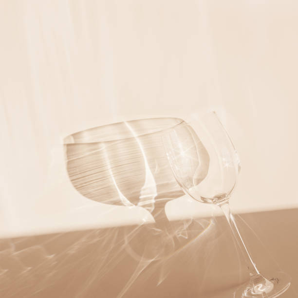istock One empty wineglass sparkling at sunlight, dark shadow and shiny reflection, sun flare light effect on table. Crystal glass top view, neutral pastel abstract beige background, copy space 2159747311